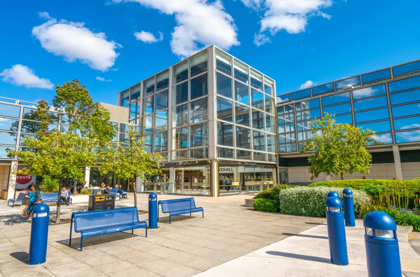 A glass-fronted building on a tree-lined pedestrian square in central Milton Keynes